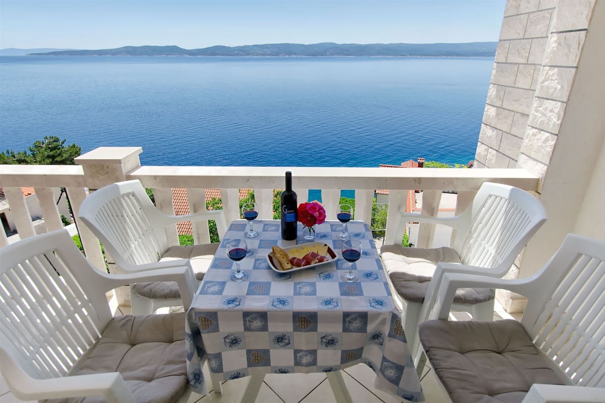 A balcony with a table set for two, overlooking a body of water.