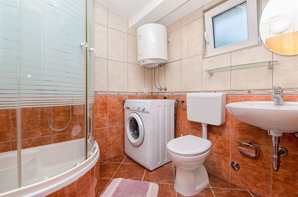 A bathroom with a glass-enclosed shower, a washing machine, a toilet, and a sink. - Apartments Bogdan (Pisak)