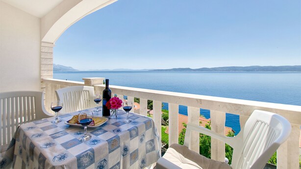 A balcony with a table set for two, overlooking a body of water and distant land. - Apartments Bogdan (Pisak)