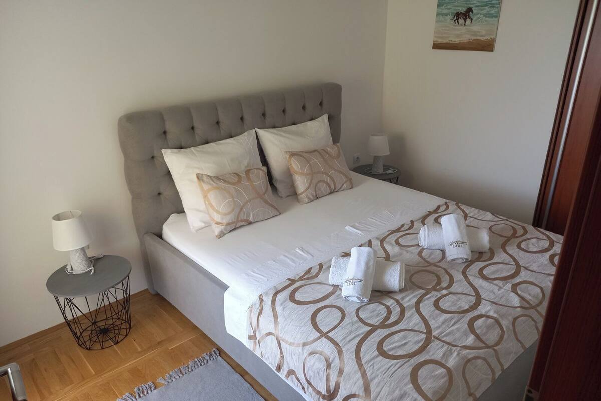 A neatly made bed with a patterned bedspread, two pillows, and rolled towels on the side.