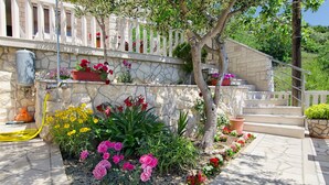 A stone staircase with a white railing leading to a balcony, surrounded by a variety of potted plants and flowers. - Apartments Bogdan (Pisak)