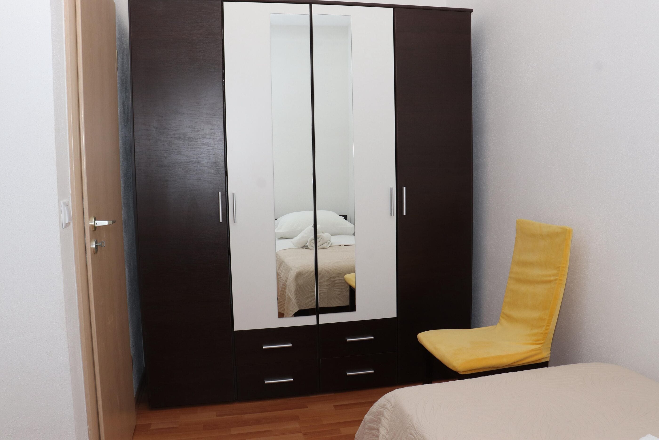 Une chambre à coucher avec une armoire, un lit et une chaise jaune.