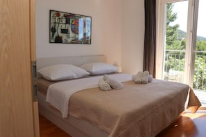 A bedroom with a bed, white pillows, a beige bedspread, and a painting on the wall. - Apartments Ena (Jelsa)