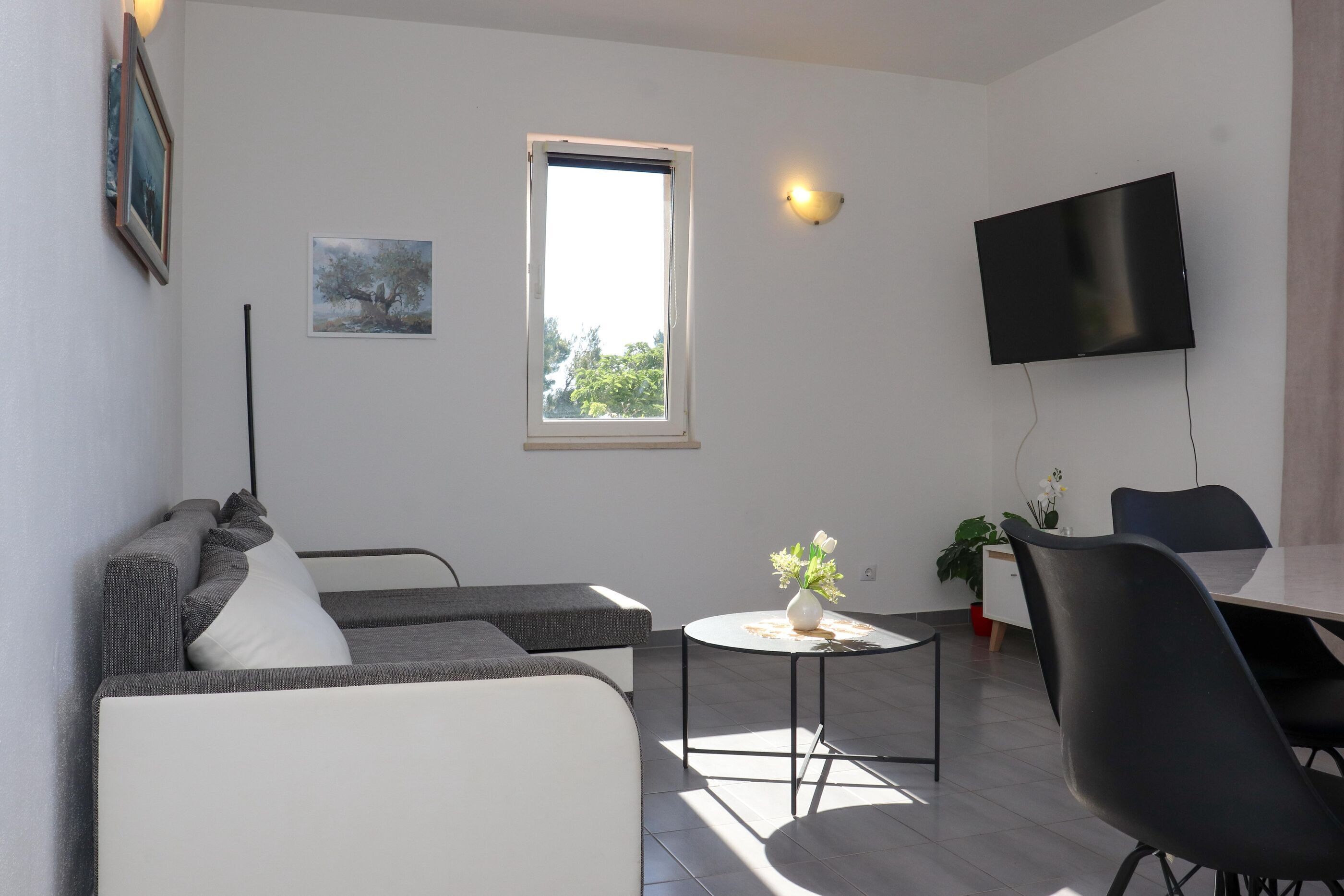 A modern living room with a sofa, a small table with a vase, a flat-screen TV, and a window.