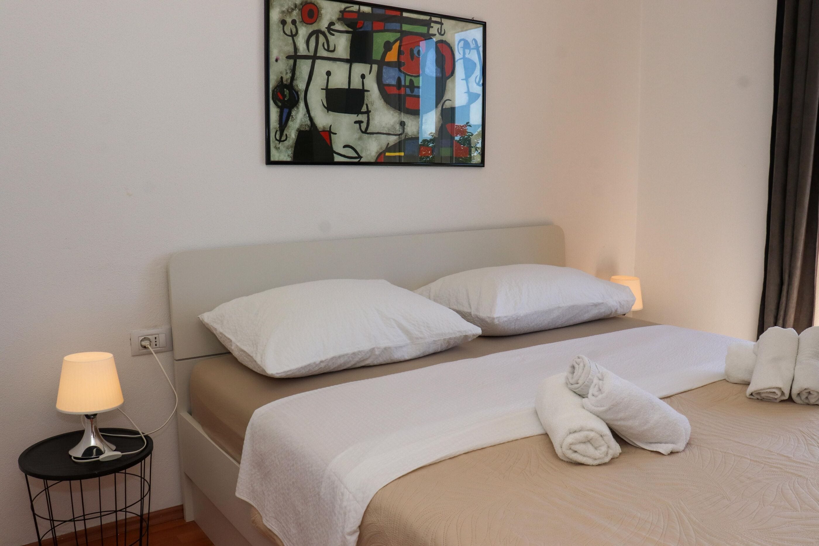 Une chambre d’hôtel avec un lit, deux lampes de chevet, un tableau au mur et des serviettes soigneusement pliées sur le lit.