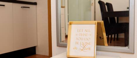 A framed inspirational quote on a white pedestal in a room with a tiled floor, a glass door, and a dining area visible through the door.