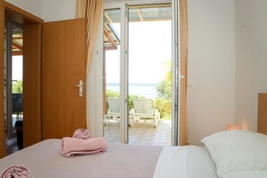 Quarto com cama, porta de madeira e vista para um pátio externo com cadeiras.
