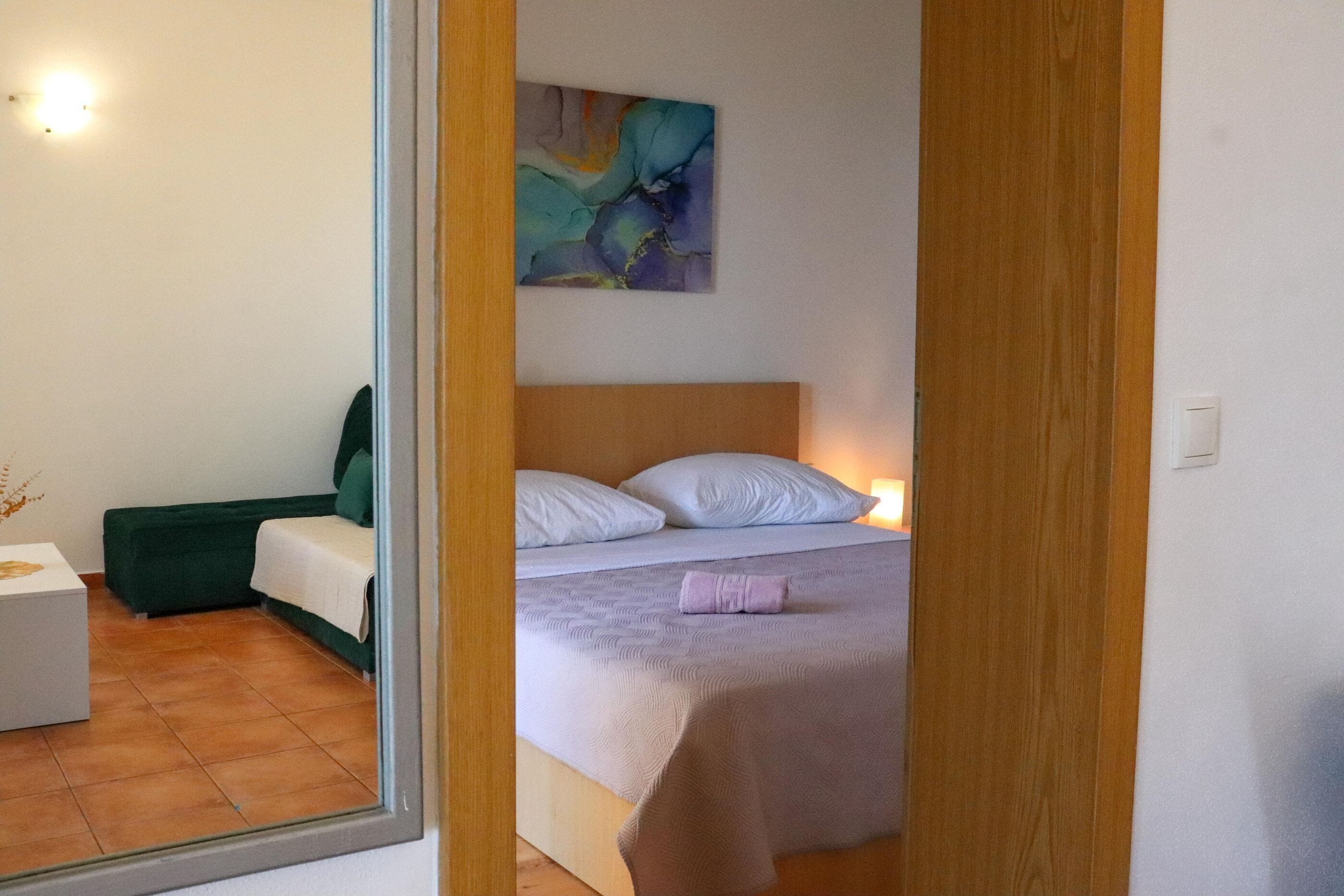 Un dormitorio con una cama, un sofá verde, una mesita de noche blanca y un cuadro en la pared.