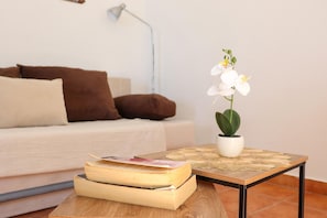 Een woonkamer met een bank, een bijzettafeltje met een boek en een potorkidee, en een lamp.