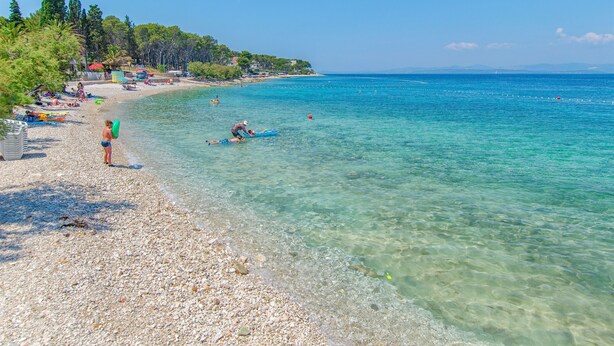 Una spiaggia con acque cristalline color turchese, un litorale di ciottoli e alcune persone che si godono il mare.