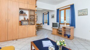Un soggiorno con TV, armadietti in legno, un tavolo da pranzo e una finestra con tende.