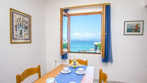 Un'area pranzo con un tavolo apparecchiato per quattro persone, una finestra con vista sul mare e due quadri appesi alle pareti.