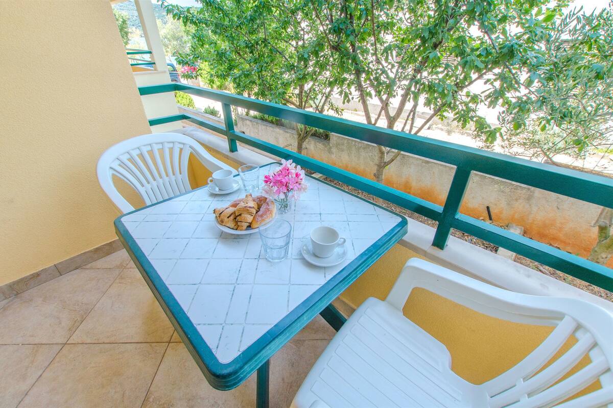 A small outdoor balcony with a table set for two, including a plate of pastries, a glass of water, and a cup.