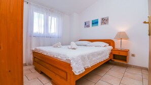 Camera da letto con un letto in legno, lenzuola bianche, un comodino con una lampada e una finestra con tende leggere.
