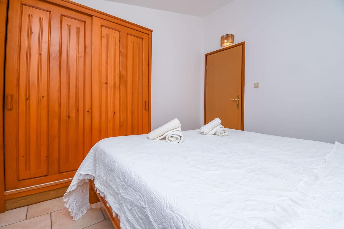 A bedroom with a large wooden wardrobe, a single bed with white bedding, and a door with a light fixture.
