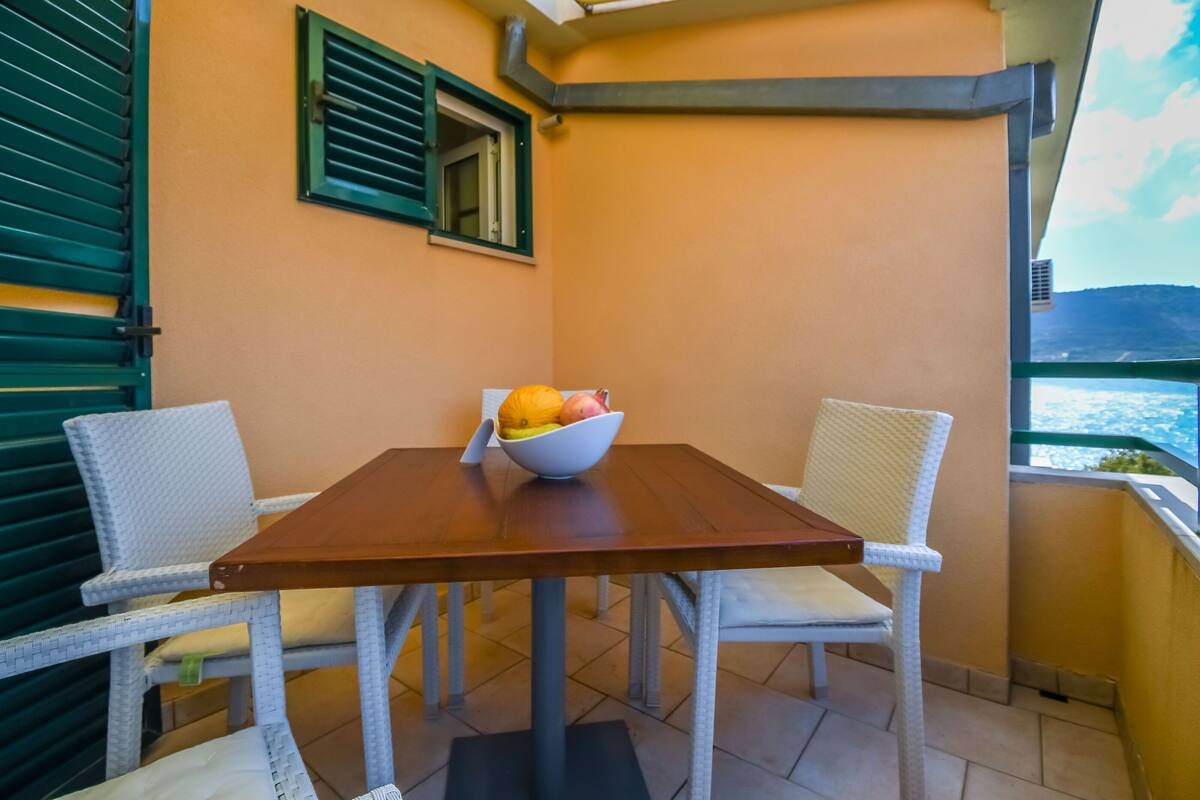 A balcony with a wooden table, two white wicker chairs, and a bowl of fruit.