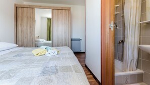 A bedroom with a bed, a wooden wardrobe, a bathroom with a shower, and a radiator. - Apartment Albina (Palit)
