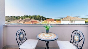A balcony with two white cushioned chairs, a small round table with a potted plant, and a tiled floor. - Apartment Albina (Palit)