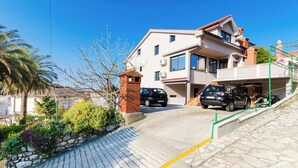 A two-story building with a brick entrance, a car parked in front, and a paved driveway leading to the entrance. - Apartment Albina (Palit)