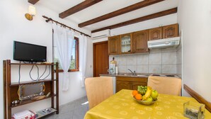 Une cuisine de taille réduite avec des meubles en bois, une table à manger recouverte d’une nappe jaune et un téléviseur posé sur un meuble en bois.