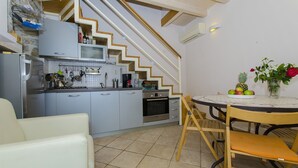 Cocina compacta con microondas, estufa y horno, una mesa de comedor con sillas, y una escalera que lleva a un nivel superior.