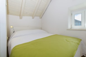 A bedroom with a bed, a window, and a ceiling with wooden beams.