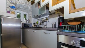 Una cocina con electrodomésticos de acero inoxidable, que incluyen un refrigerador, un microondas y un horno. Hay armarios con manijas, un lavamanos y un escurreplatos.