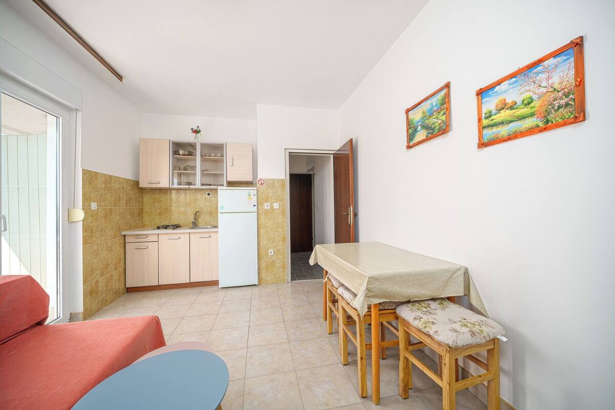 A compact kitchen with a dining area, a small table with chairs, and two framed pictures on the wall.