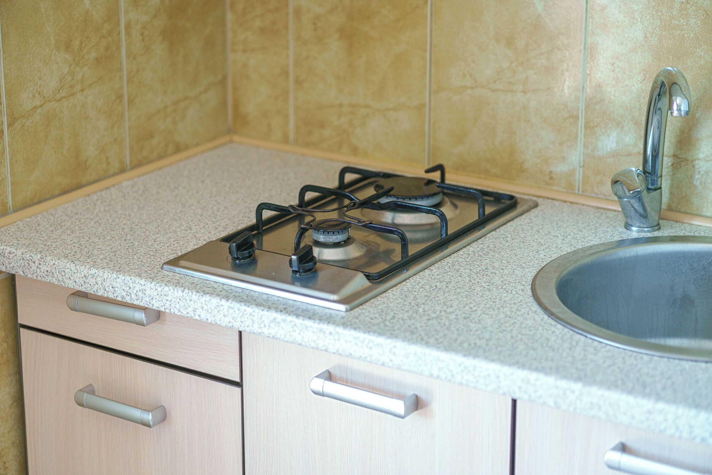 A kitchen with a gas stove, a sink, and light-colored cabinets.