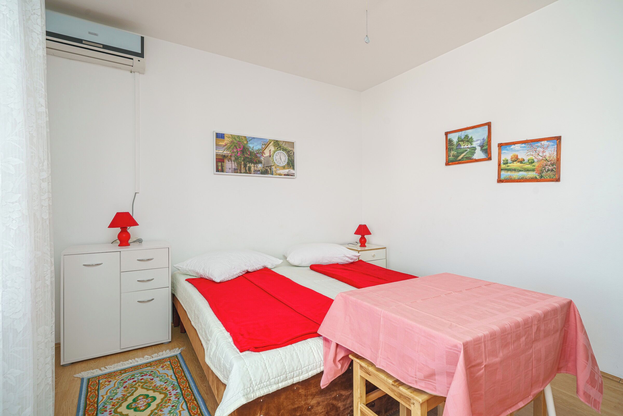 Ein Schlafzimmer mit zwei Betten, einem Schreibtisch und einem Stuhl. An den Wänden hängen zwei Gemälde.
