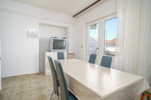 A dining area with a table, chairs, a television on a small cabinet, and a view through a glass door. - Apartments and Rooms Josipa (Vodice)
