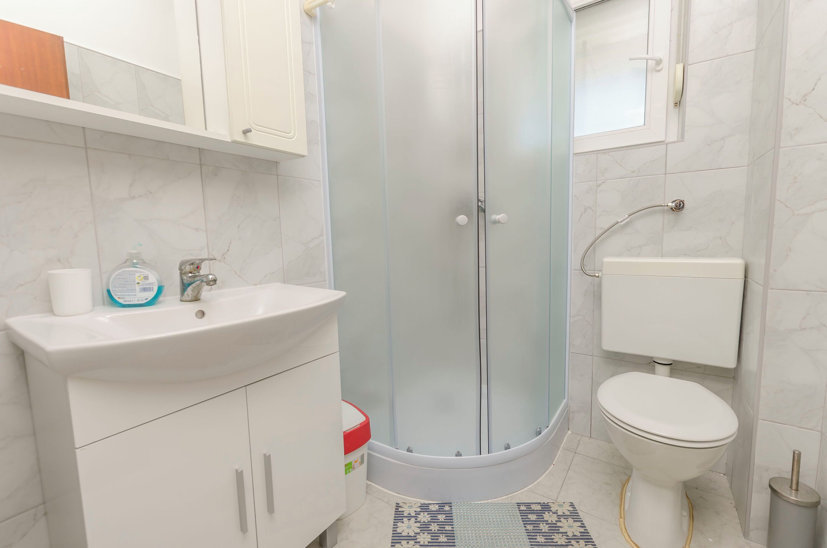 A bathroom with a glass-enclosed shower, a white sink, a toilet, and a small rug on the floor.
