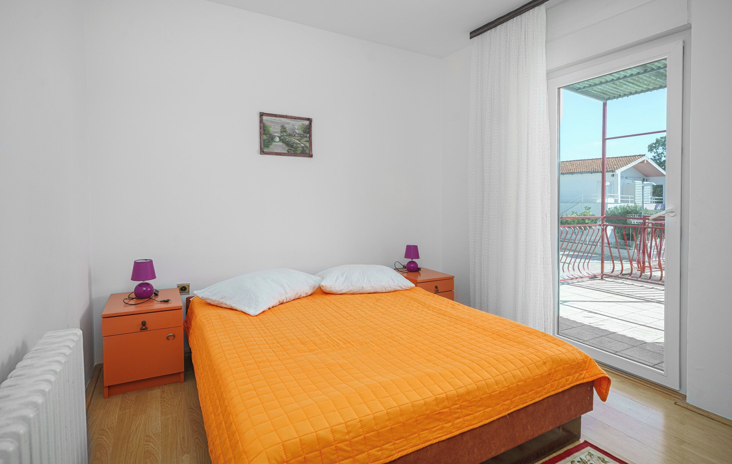A bedroom with a bed, two nightstands, a window with a view, and a small picture on the wall.