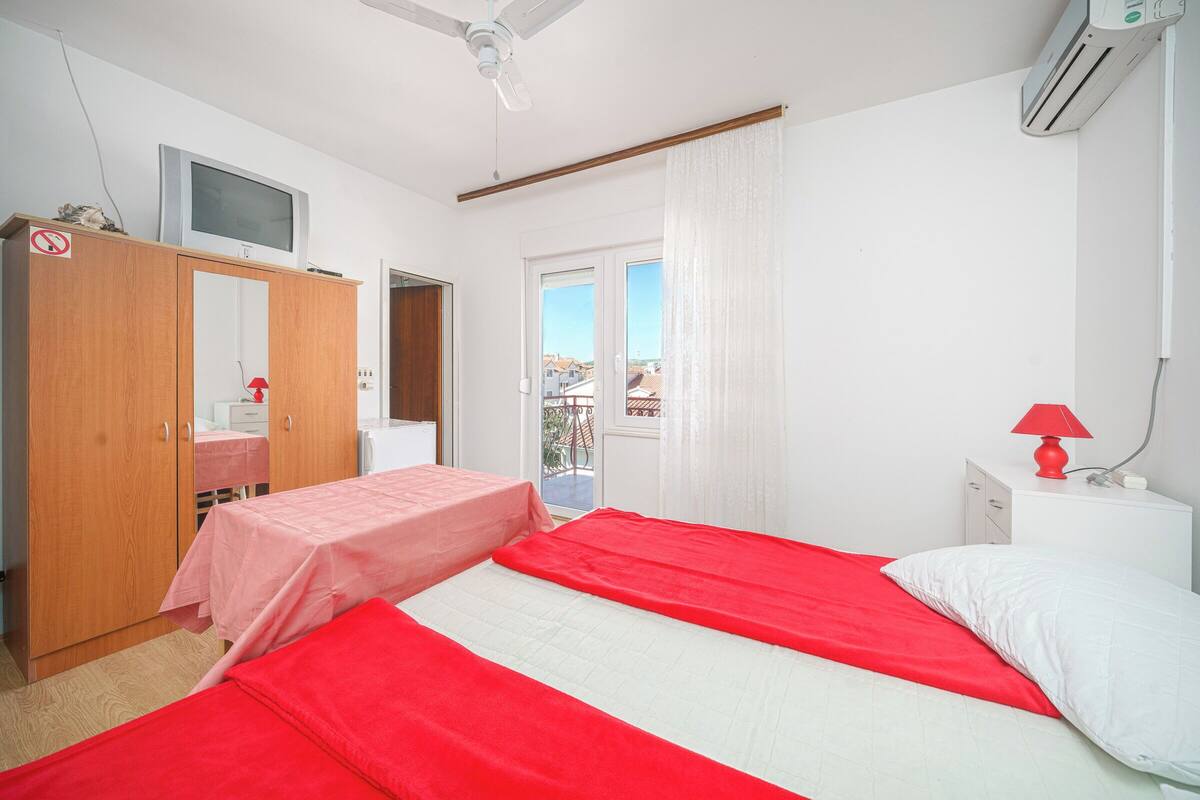 A bedroom with two beds, a wardrobe, a television, and a window with curtains.