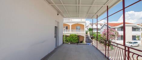 Un balcón techado con baranda metálica, vista a casas vecinas y cielo despejado.