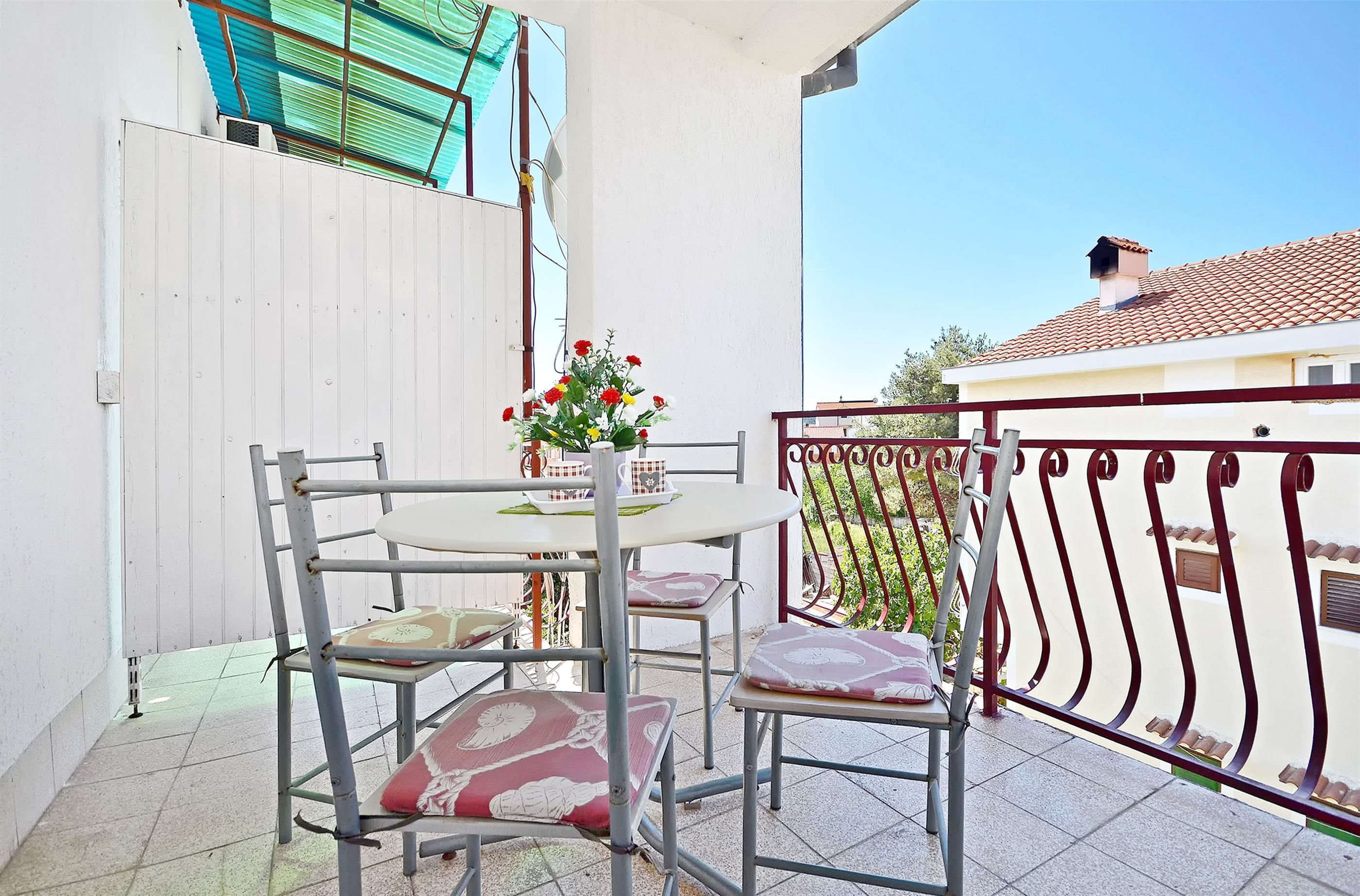 Un balcon avec une table et des chaises, un vase à fleurs et une rambarde en métal.