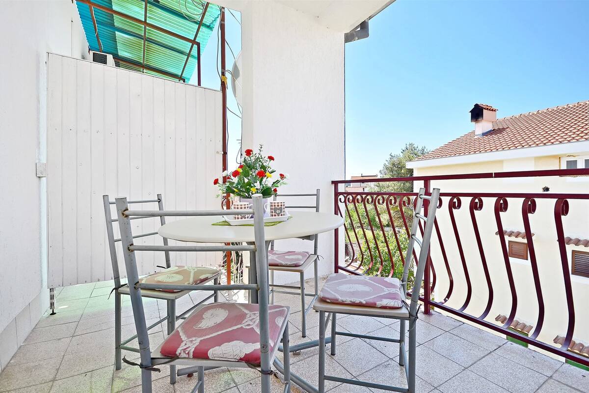A balcony with a table and chairs, a flower vase, and a metal railing.