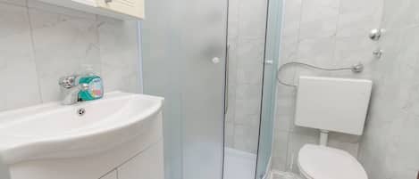 Une salle de bain avec une douche à parois de verre, un lavabo blanc et des toilettes.