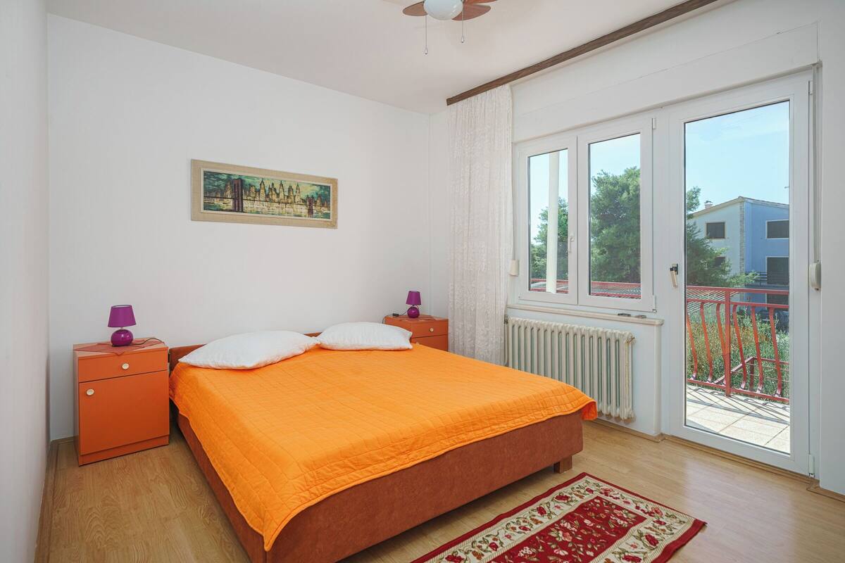 A bedroom with a large bed, a nightstand, a window with a view, and a ceiling fan.