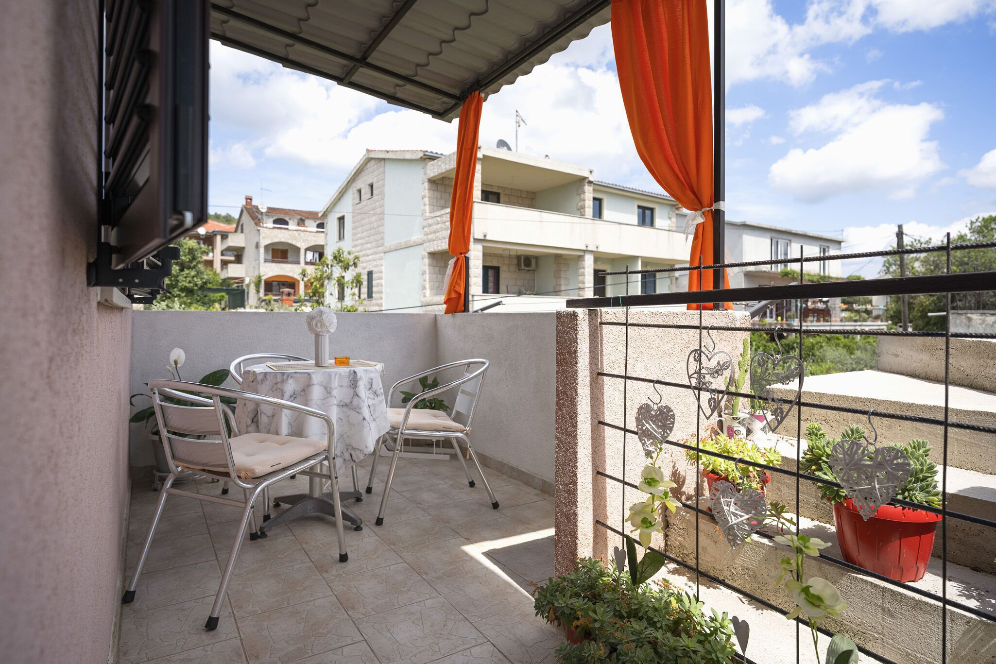 A balcony with a table and chairs, potted plants, and a view of buildings in the background.