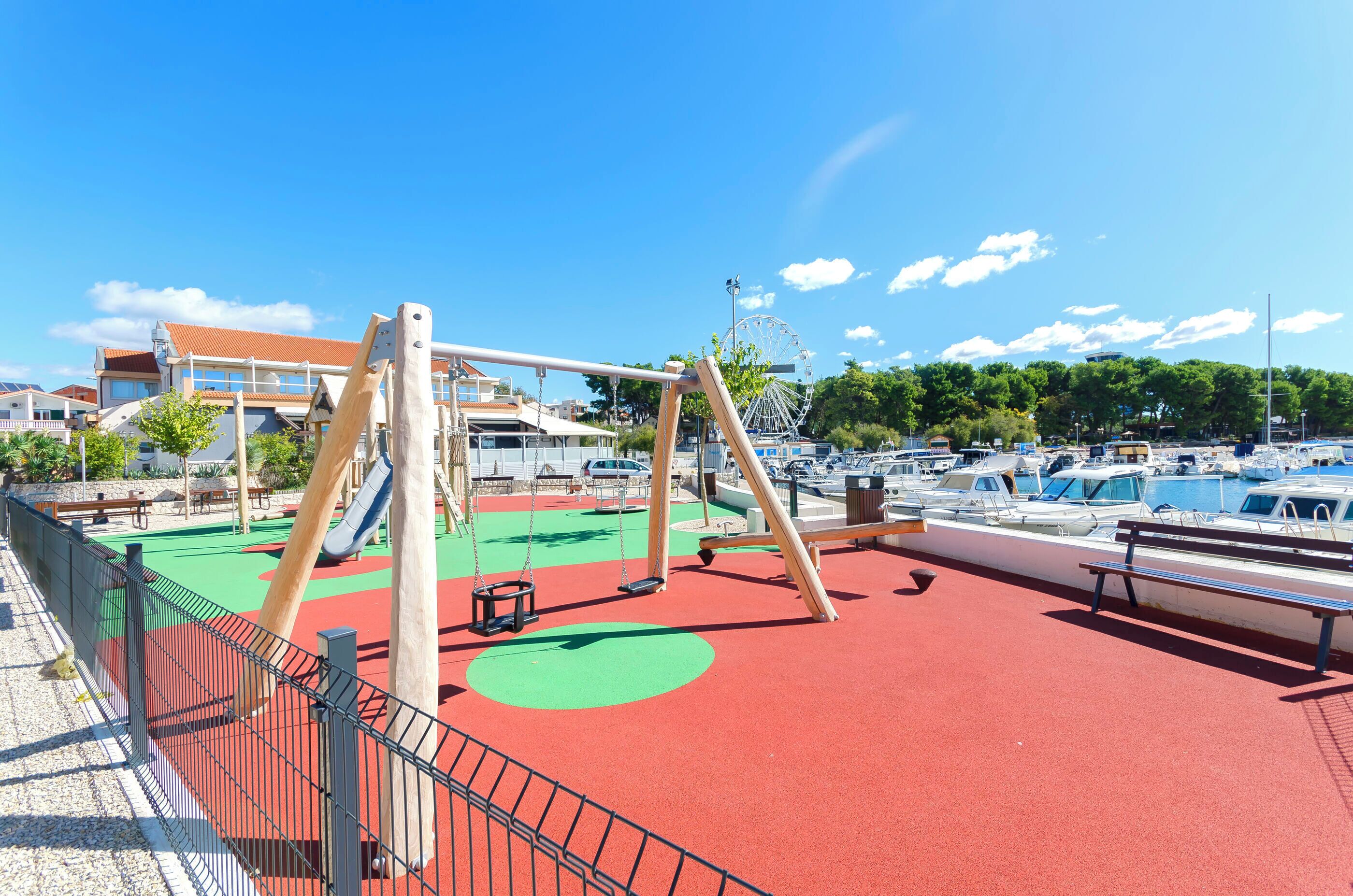 A playground with swings and a slide, a Ferris wheel, and a marina with boats.