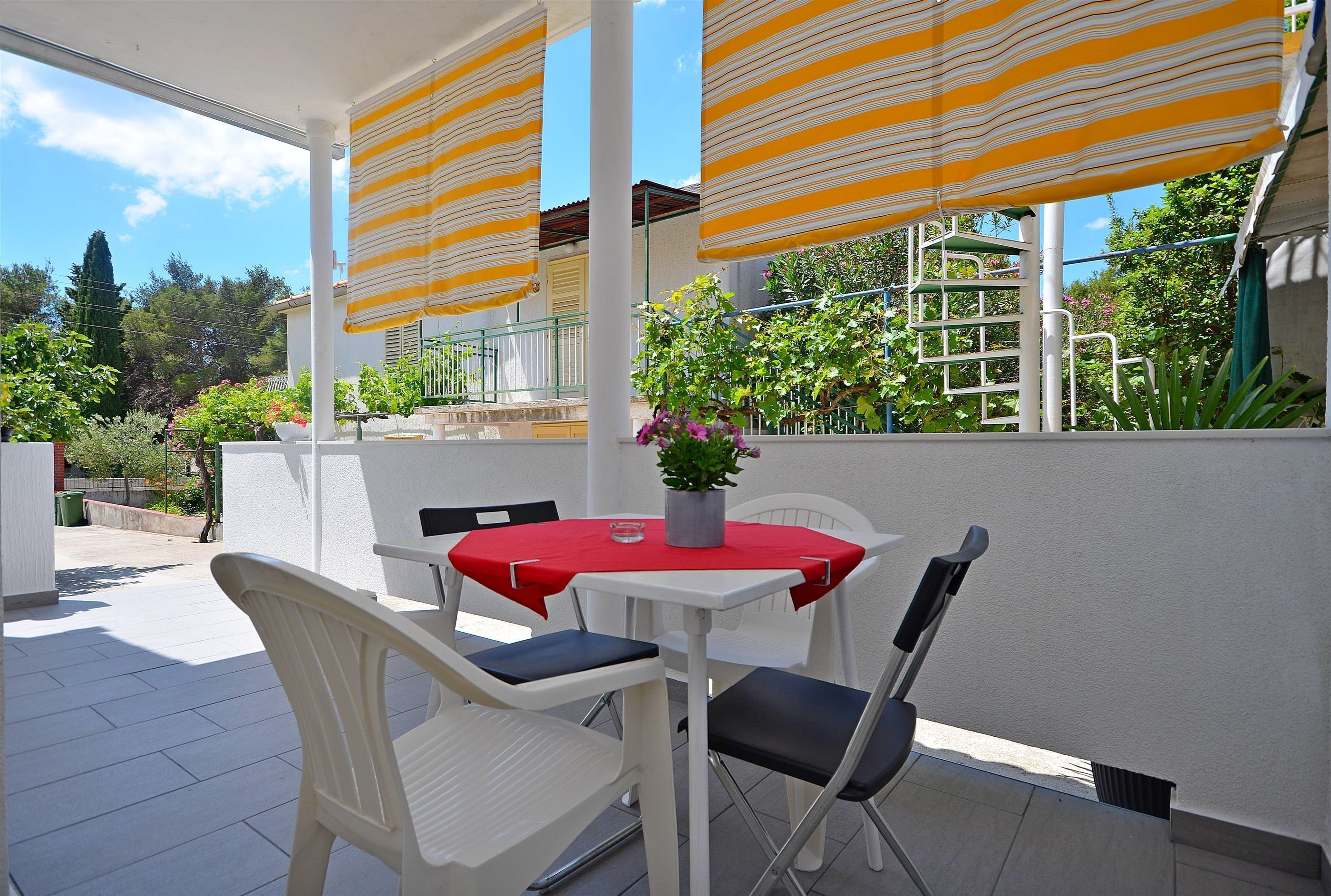 Eine überdachte Terrasse mit Tisch und Stühlen, einem Blumentopf und Blick auf eine Wohngegend.