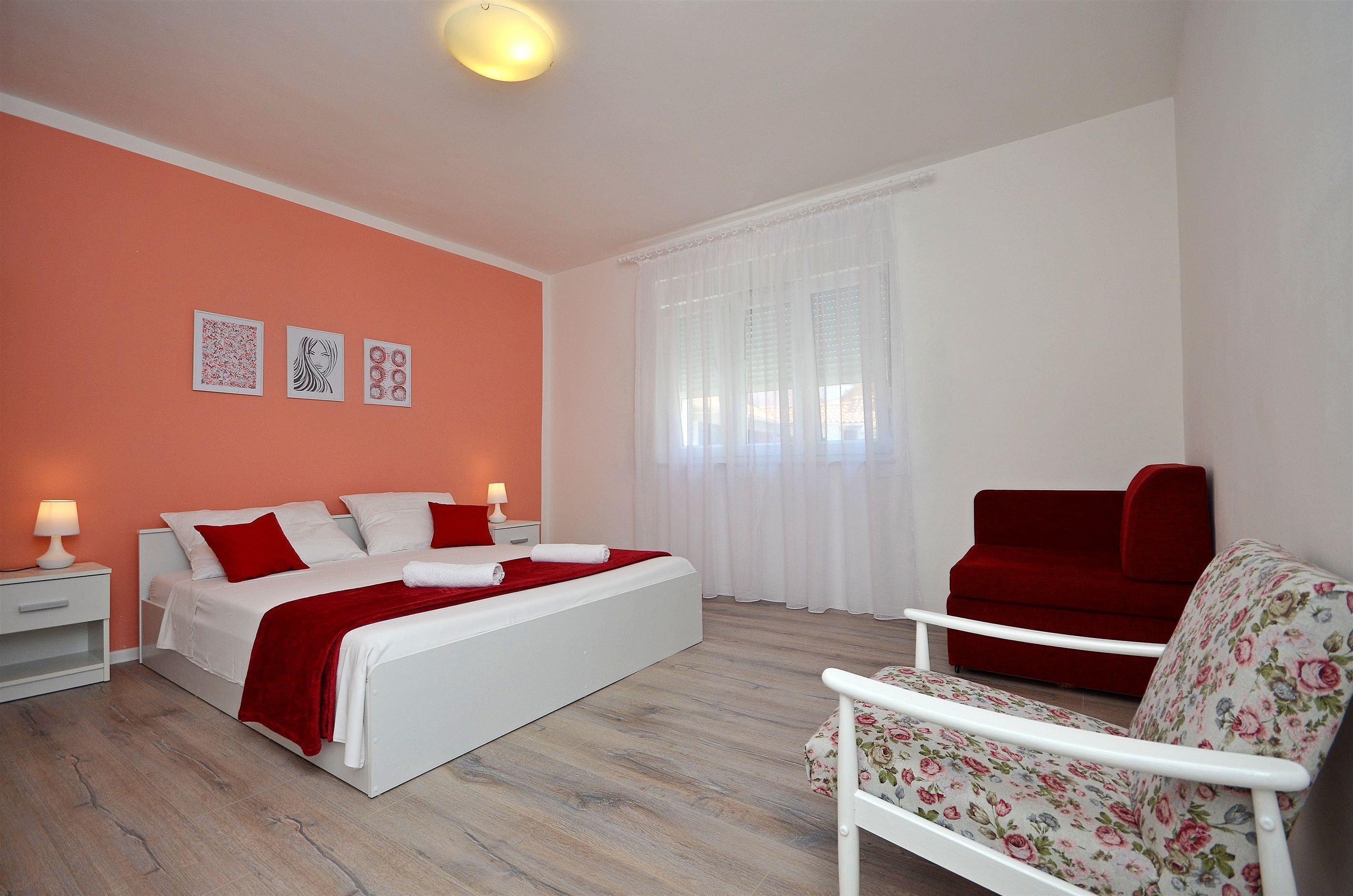 A bedroom with a bed, a red chair, and a nightstand with a lamp.
