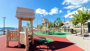 A playground with wooden climbing structures and a slide, surrounded by a red and green play area, benches, and trees. - Apartment Ines (Vodice)