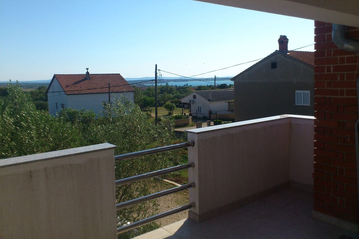 A balcony with a metal railing overlooking a residential area with houses and a clear sky.