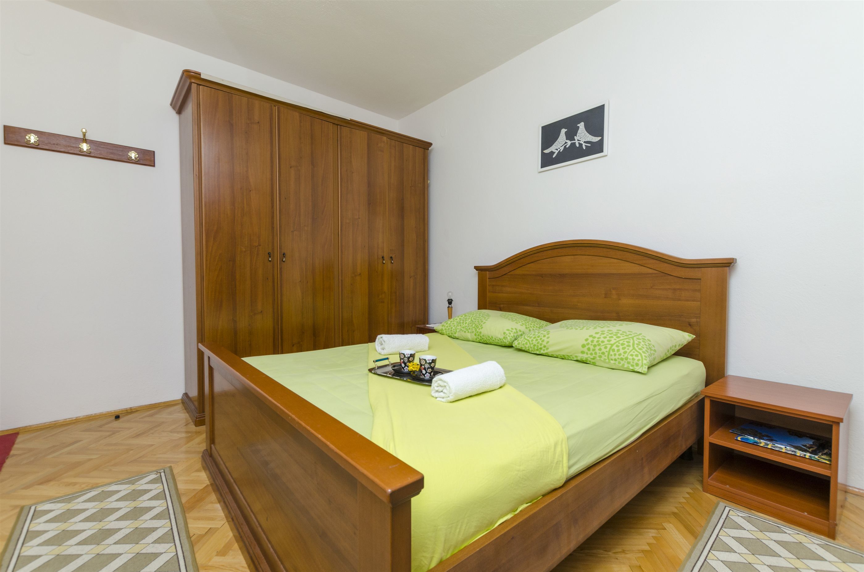 A neatly made bed with green bedding, a wooden headboard, and a small wooden nightstand beside it.