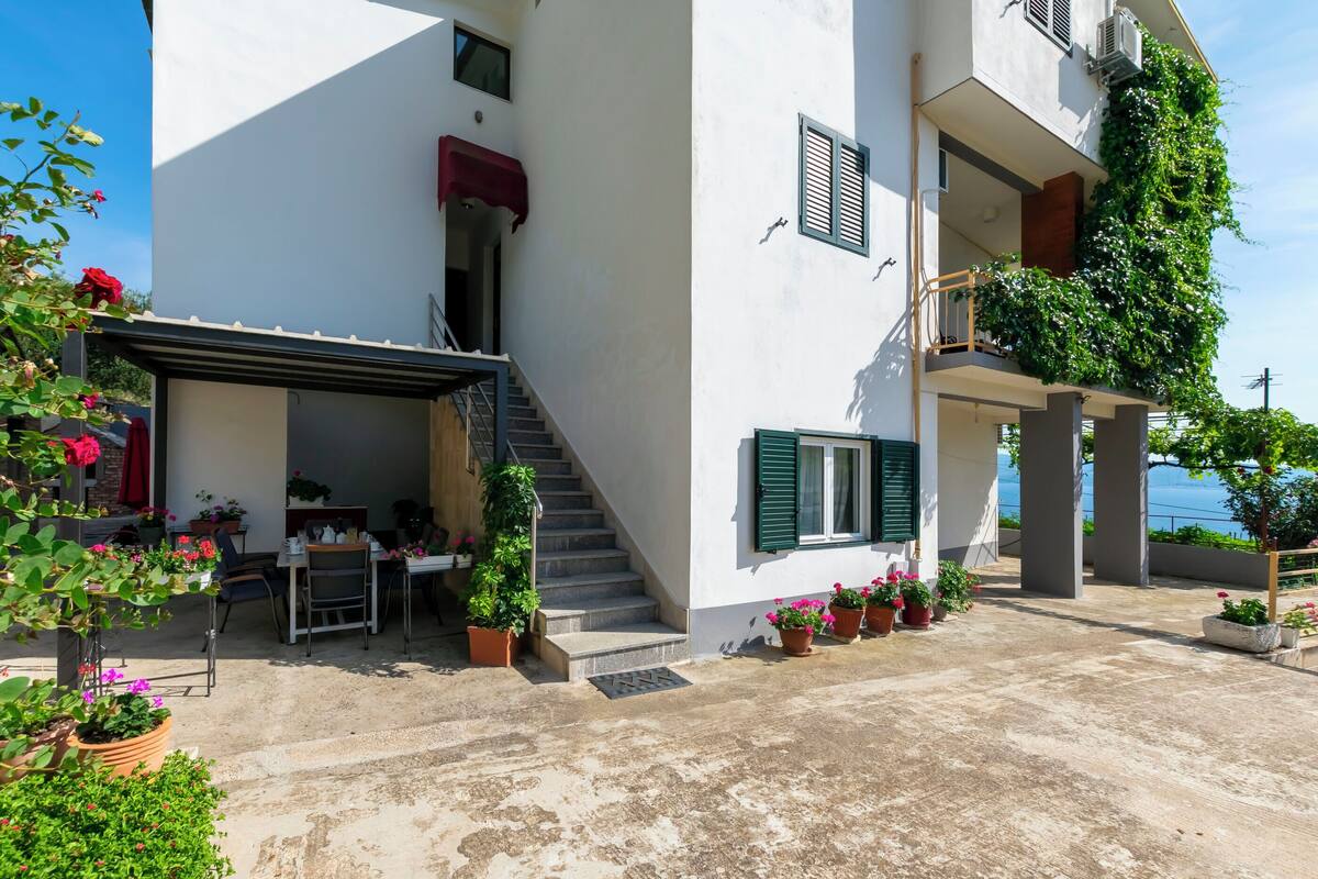 A two-story building with a covered outdoor seating area, a staircase, and potted plants.