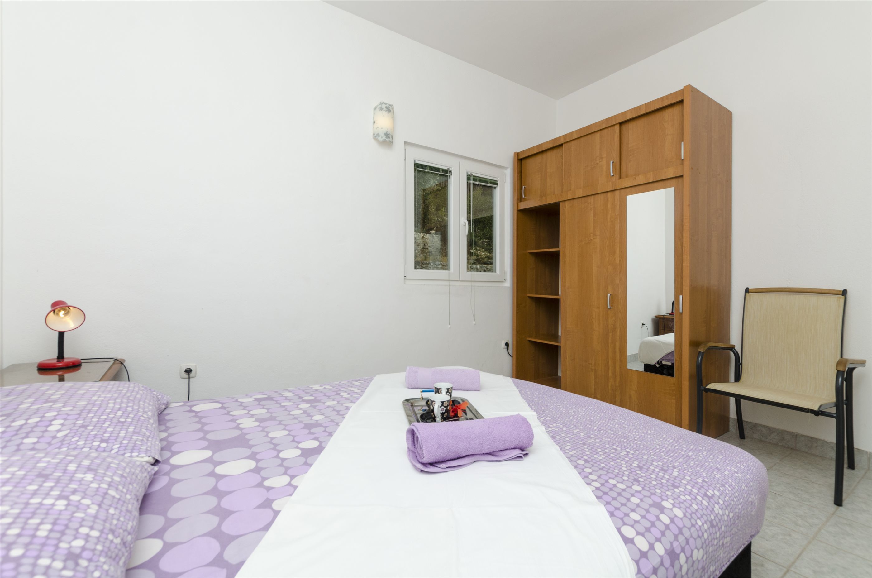 Un dormitorio con cama, armario, silla y mesita de noche con lámpara.