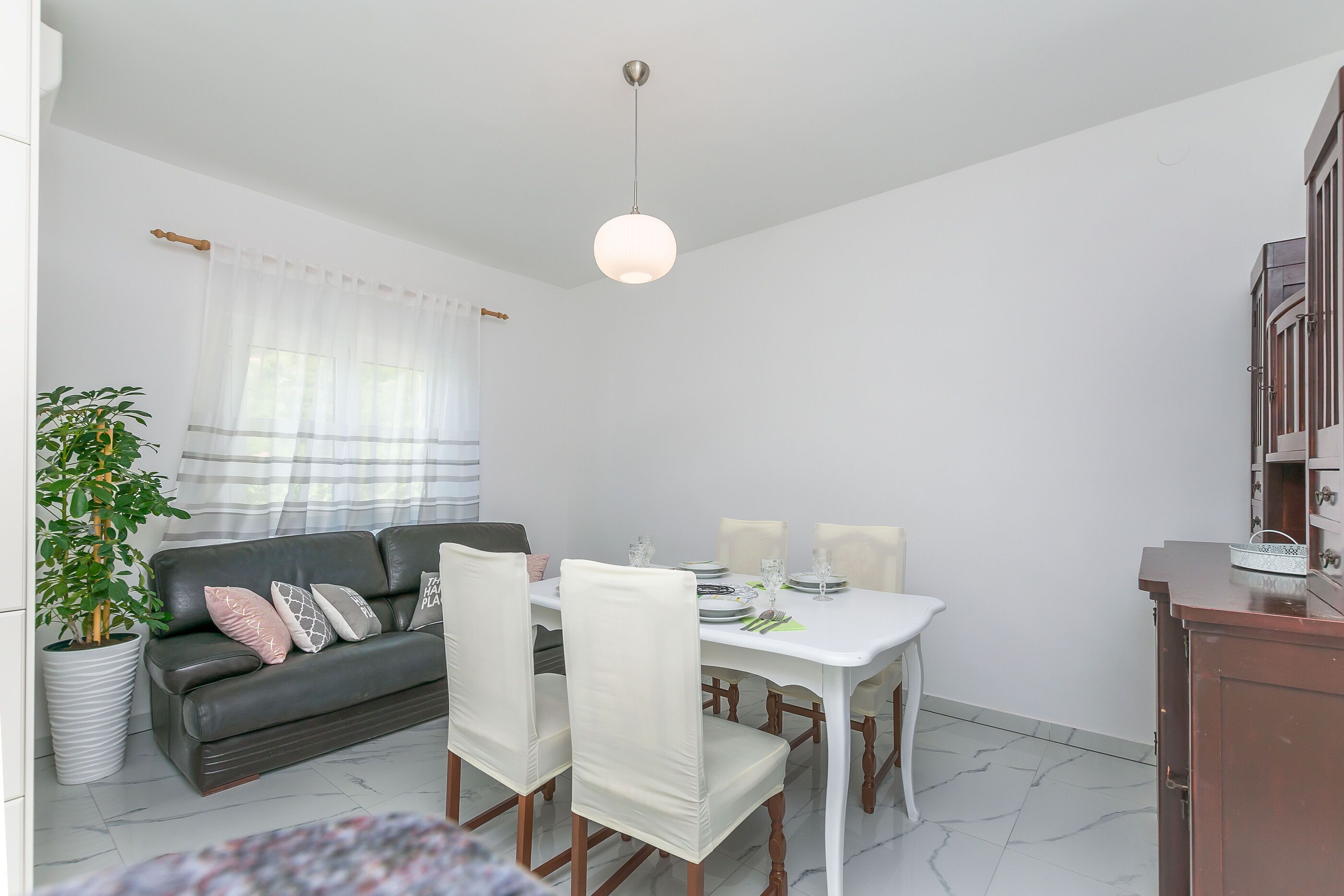 A dining area with a white table, four chairs, and a hanging light fixture.