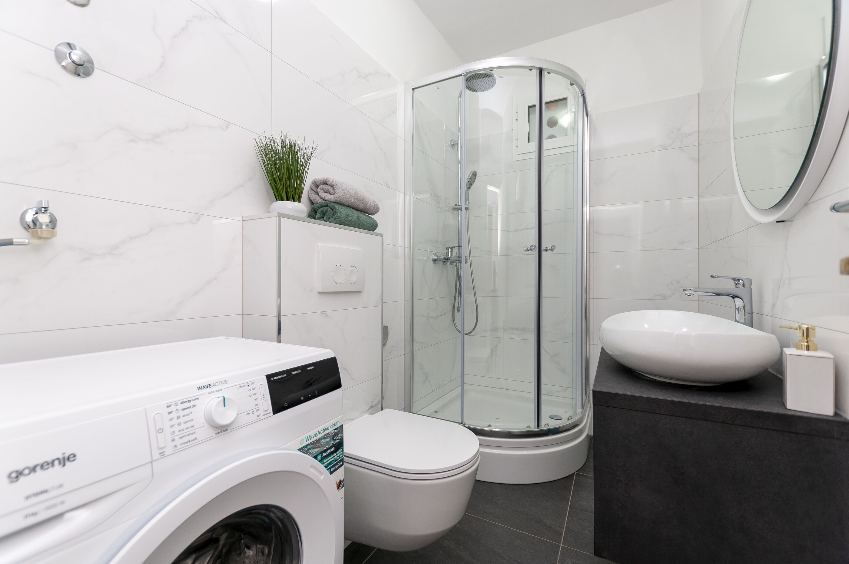 Ein modernes Badezimmer mit Waschmaschine, Toilette, Duschkabine und Waschbecken.